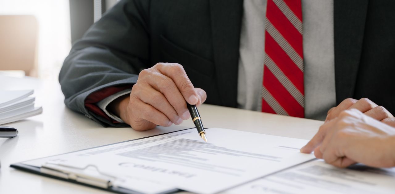 Symbolbild für AGB: Eine Person zeigt mit einem Stift auf eine Seite mit Text, die vor ihr liegt