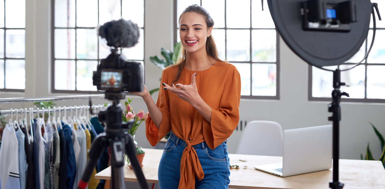 Influencerin steht vor Kamera und spricht in Mikrofon, während sie einen Vlog aufnimmt – professionelles Setting mit Ringlicht und Laptop im Hintergrund.